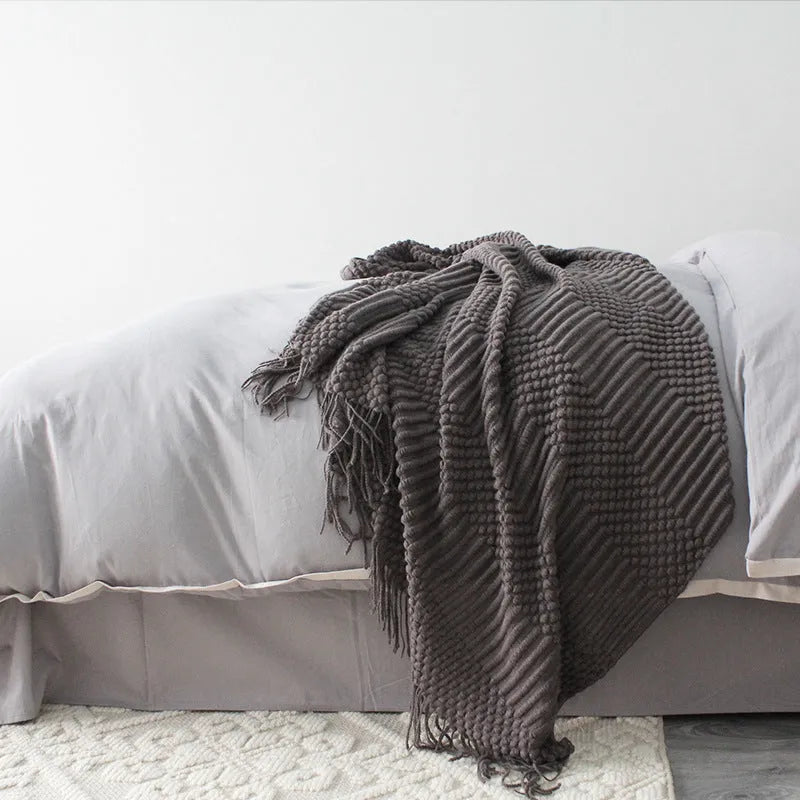 Small rectangular polyester nap blanket in neutral colour on a sofa, showing its 127 cm by 170 cm size.