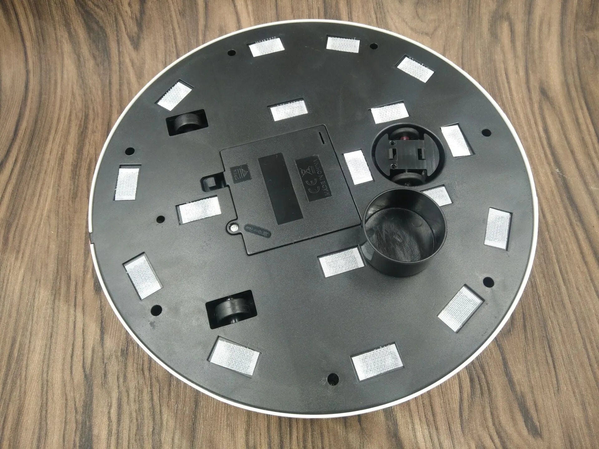 Black or white AC-powered robot vacuum cleaner on a wooden floor.
