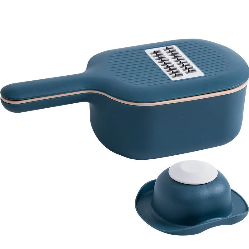 Dark blue vegetable cutter with four stainless steel blades, drain basket, and hand guard on a kitchen counter.