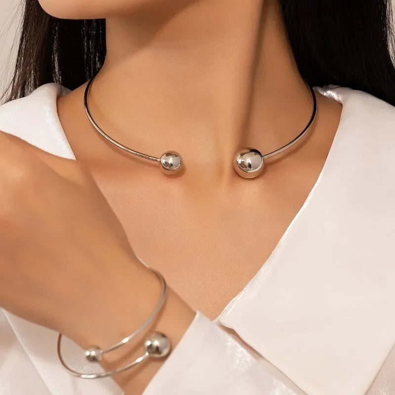 Gold dislocation ball open-end thin bangle bracelet with matching necklace on a flat surface