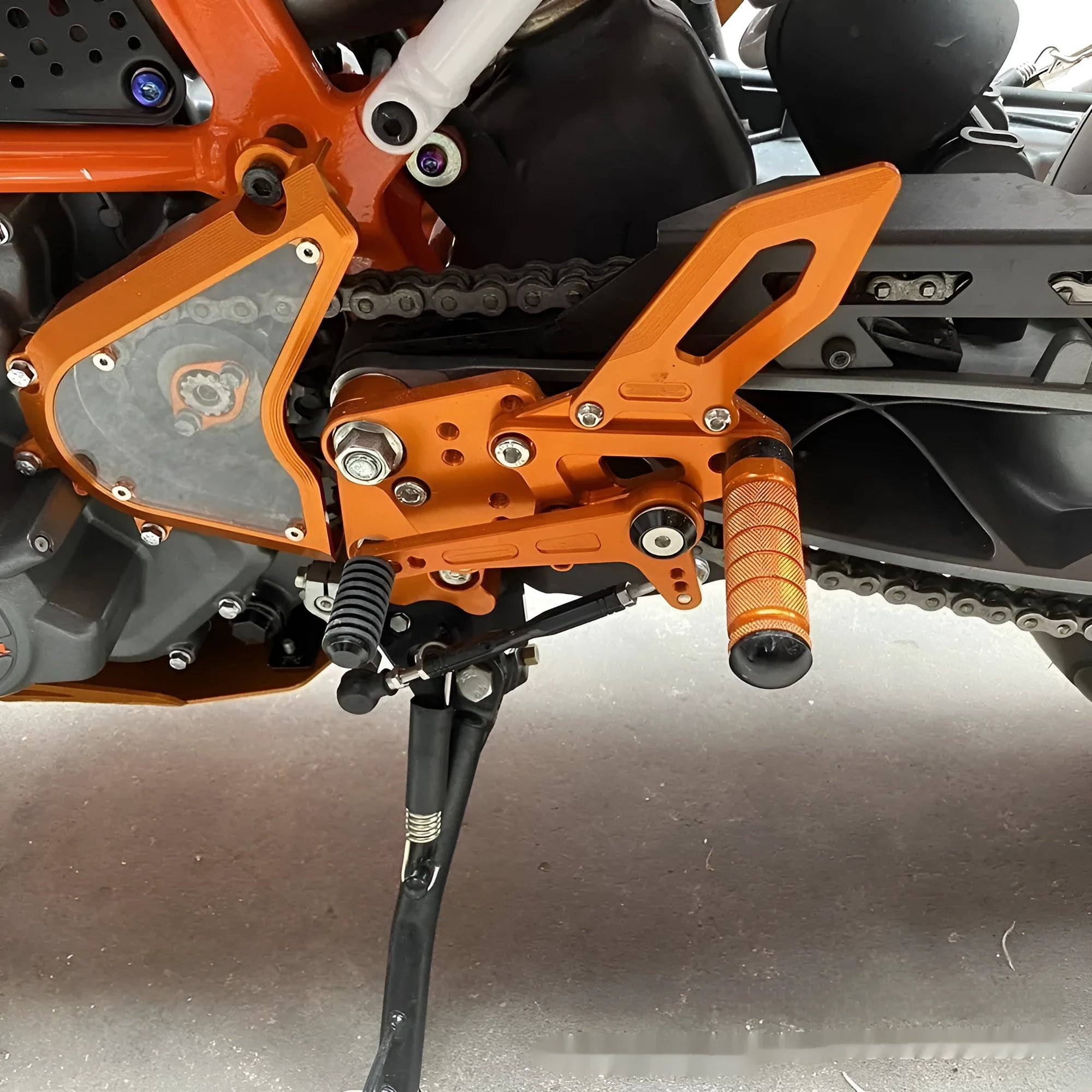 Black and orange KTM Duke motorcycle raised footrest bracket assembly