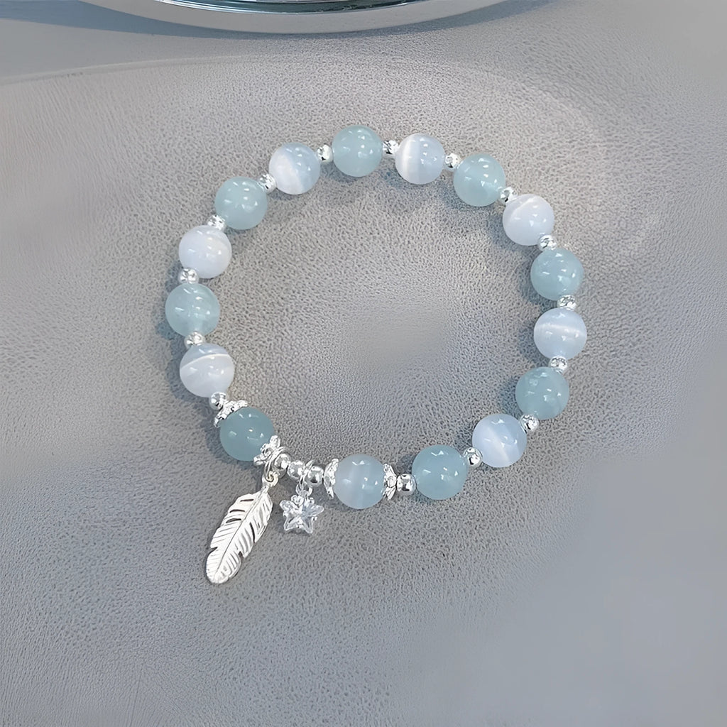 Small white crystal and glass charm bracelet with feather and blue moonlight details on wrist.