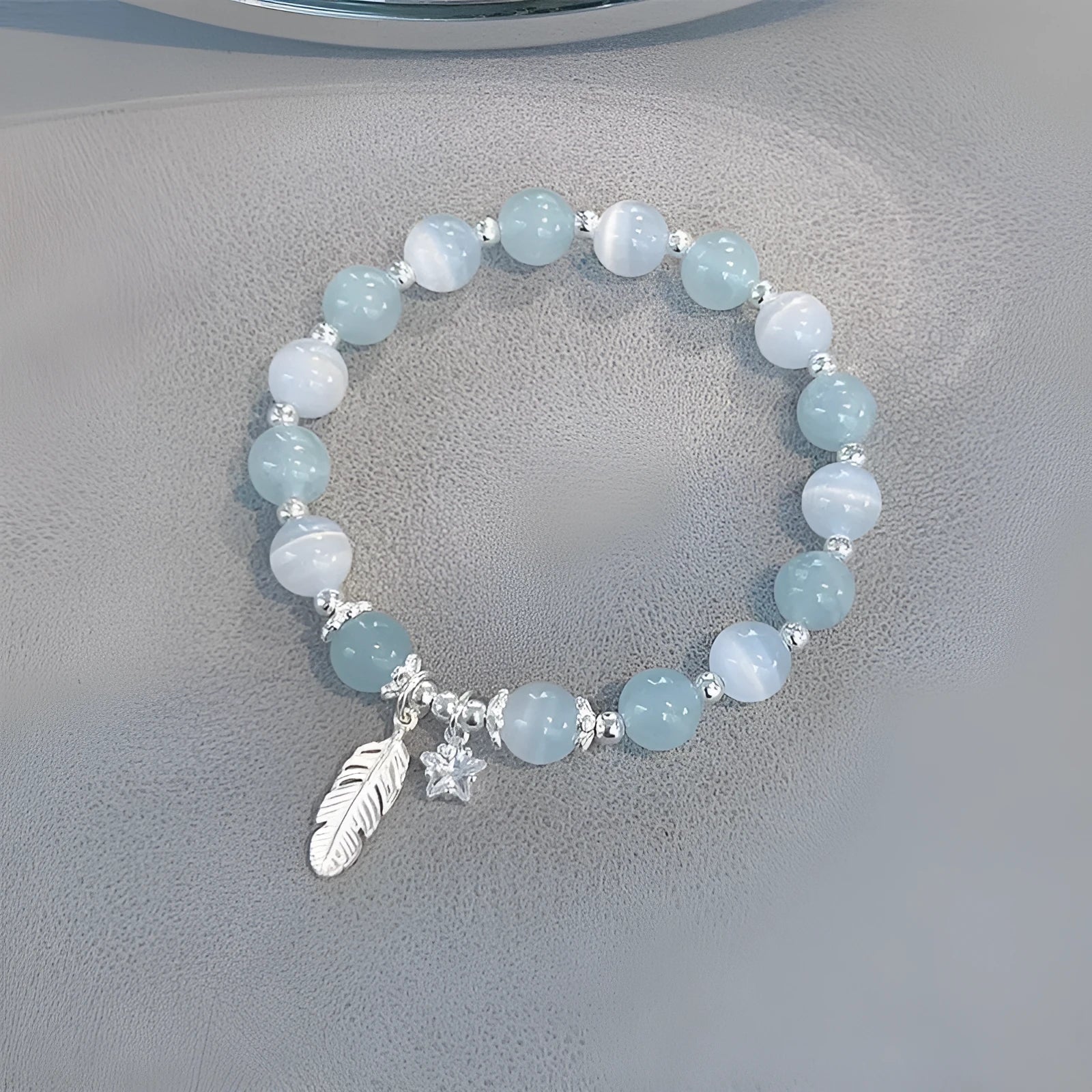 Small white crystal and glass charm bracelet with feather and blue moonlight details on wrist.