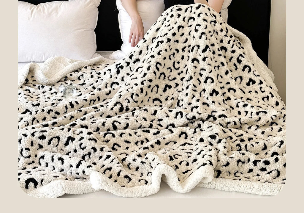 Double-layer taffeta blanket with reversible leopard jacquard print in camel colour, laid over a sofa.