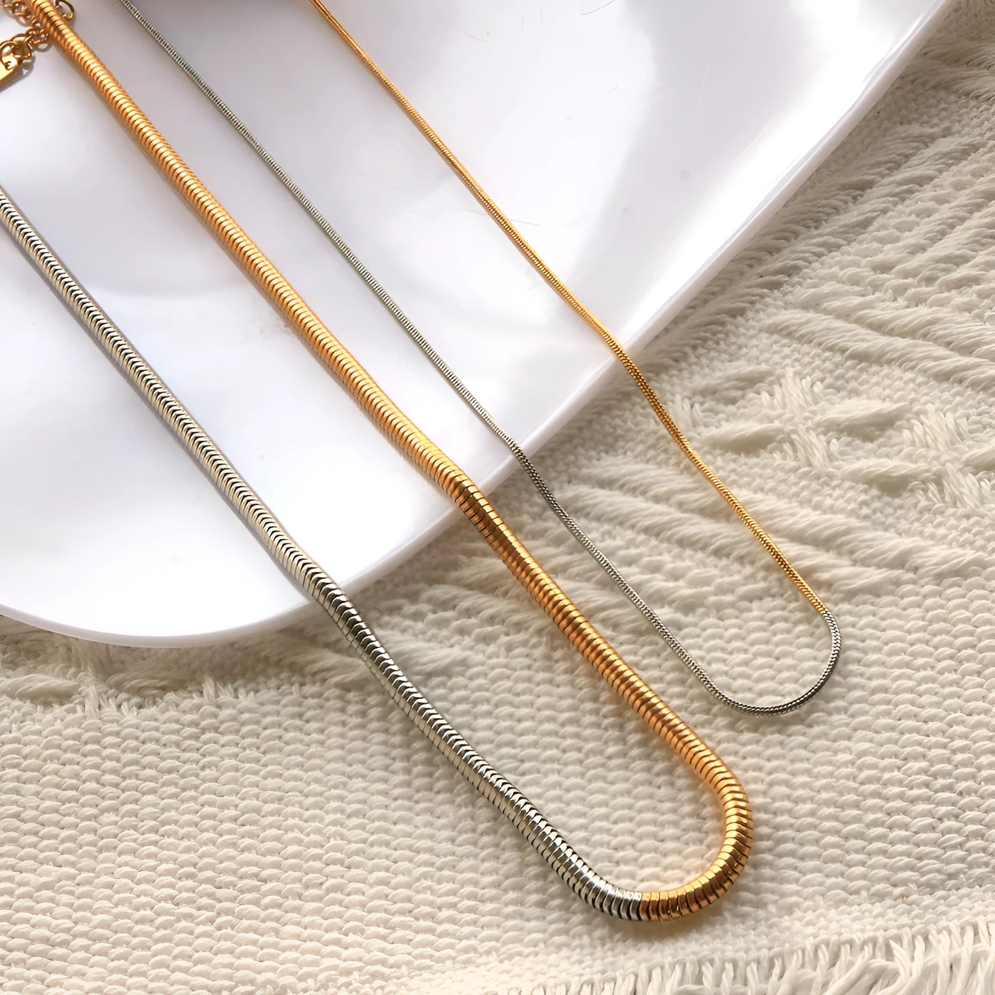 Cold golden 3mm wide stainless steel snake bones chain necklace on a flat surface.