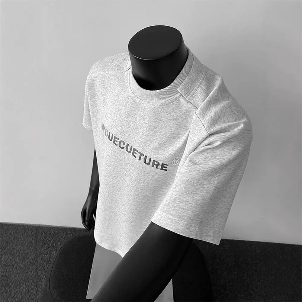Man wearing a light grey short sleeve pullover shirt with a loose fit and black letter graphic.