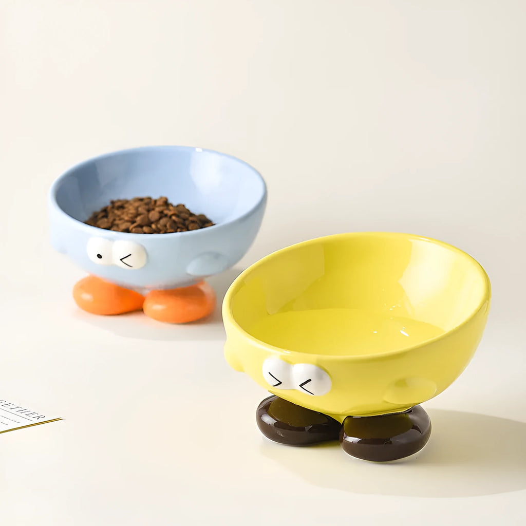Blue and yellow ceramic slanted pet food bowls with animal face expressions for cervical spine support.