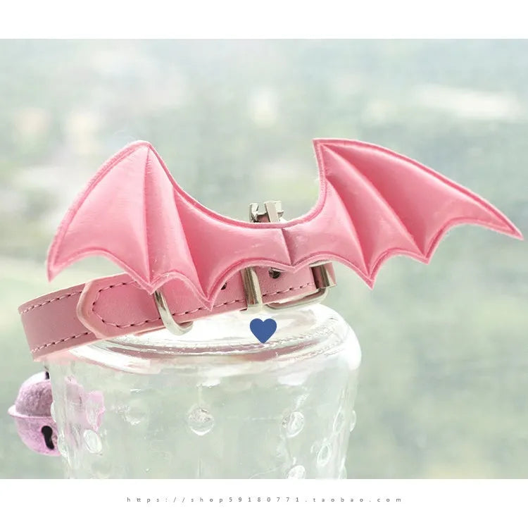 Small black patent leather pet collar with silver devil wings charm and bell on a white background.