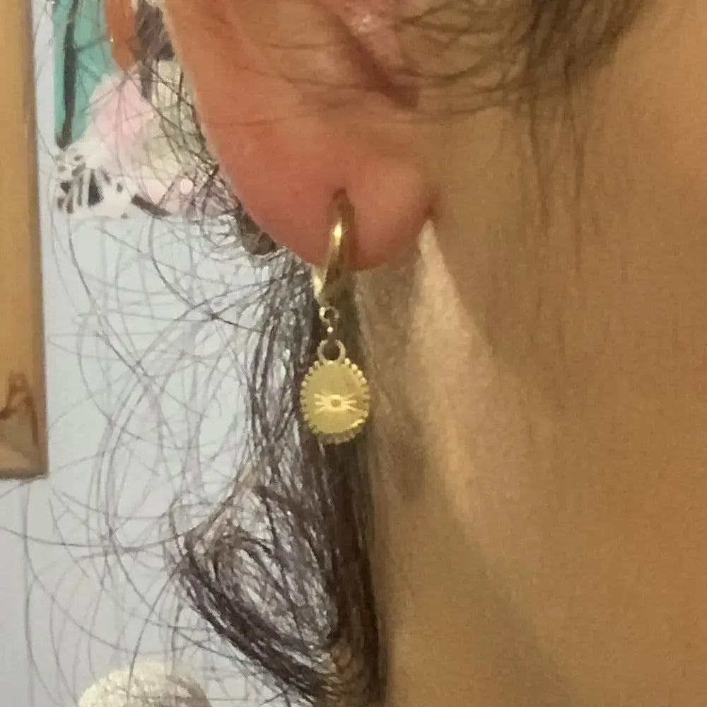 A pair of stainless steel geometric earrings featuring a central ellipse design on a woman's ear.