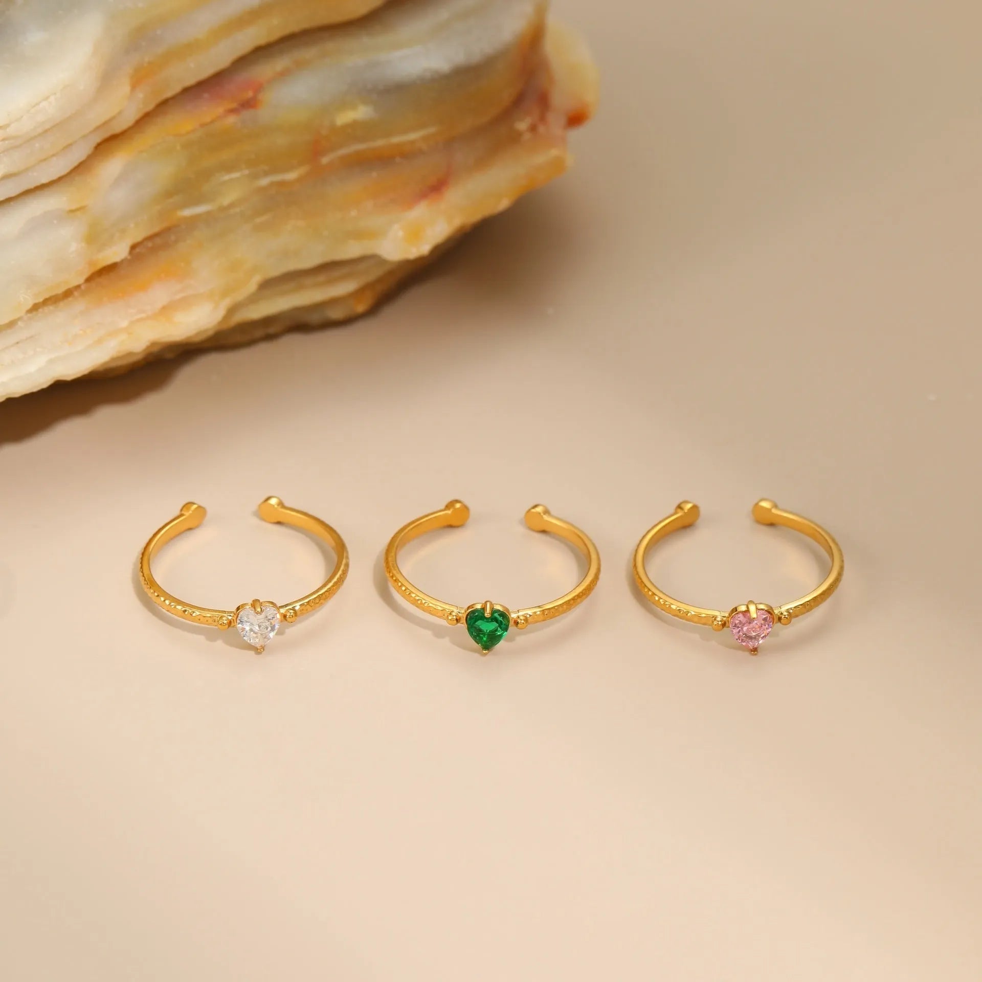 Open-ended geometric stainless steel ring with a heart-shaped green zirconium inlay on a grey background.