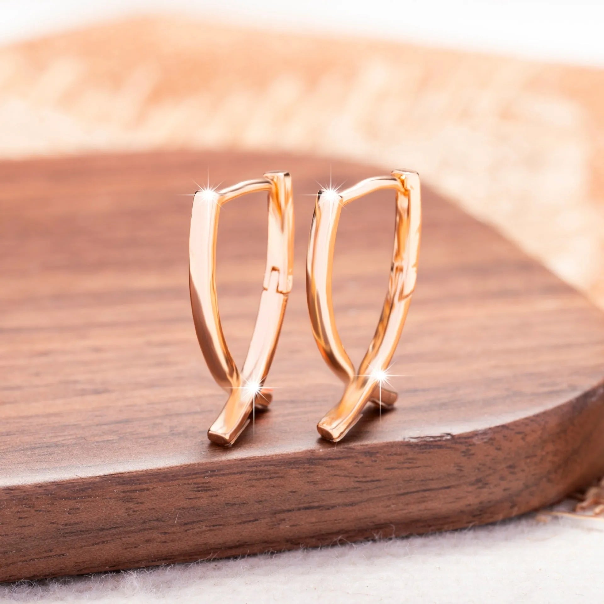 A pair of rose gold cross shaped earrings made from copper on a plain background.