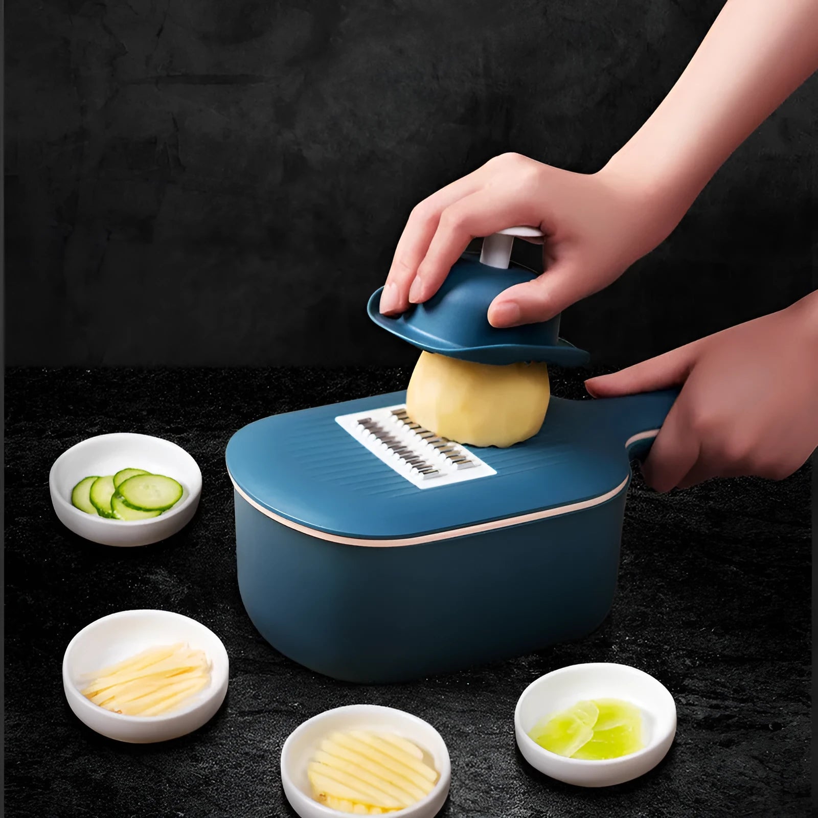 Dark blue vegetable cutter with four stainless steel blades, drain basket, and hand guard on a kitchen counter.