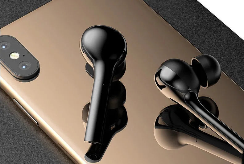 Black and white wireless in-ear Bluetooth headphones with a charging case on a table.