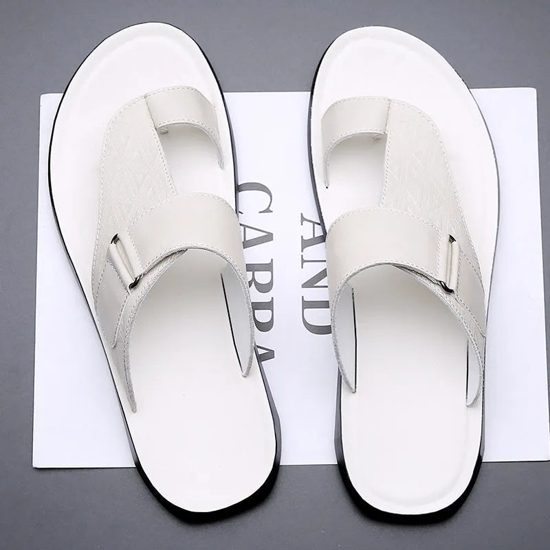 Men's white cowhide open-toe beach slippers with a rubber sole on a sandy background.