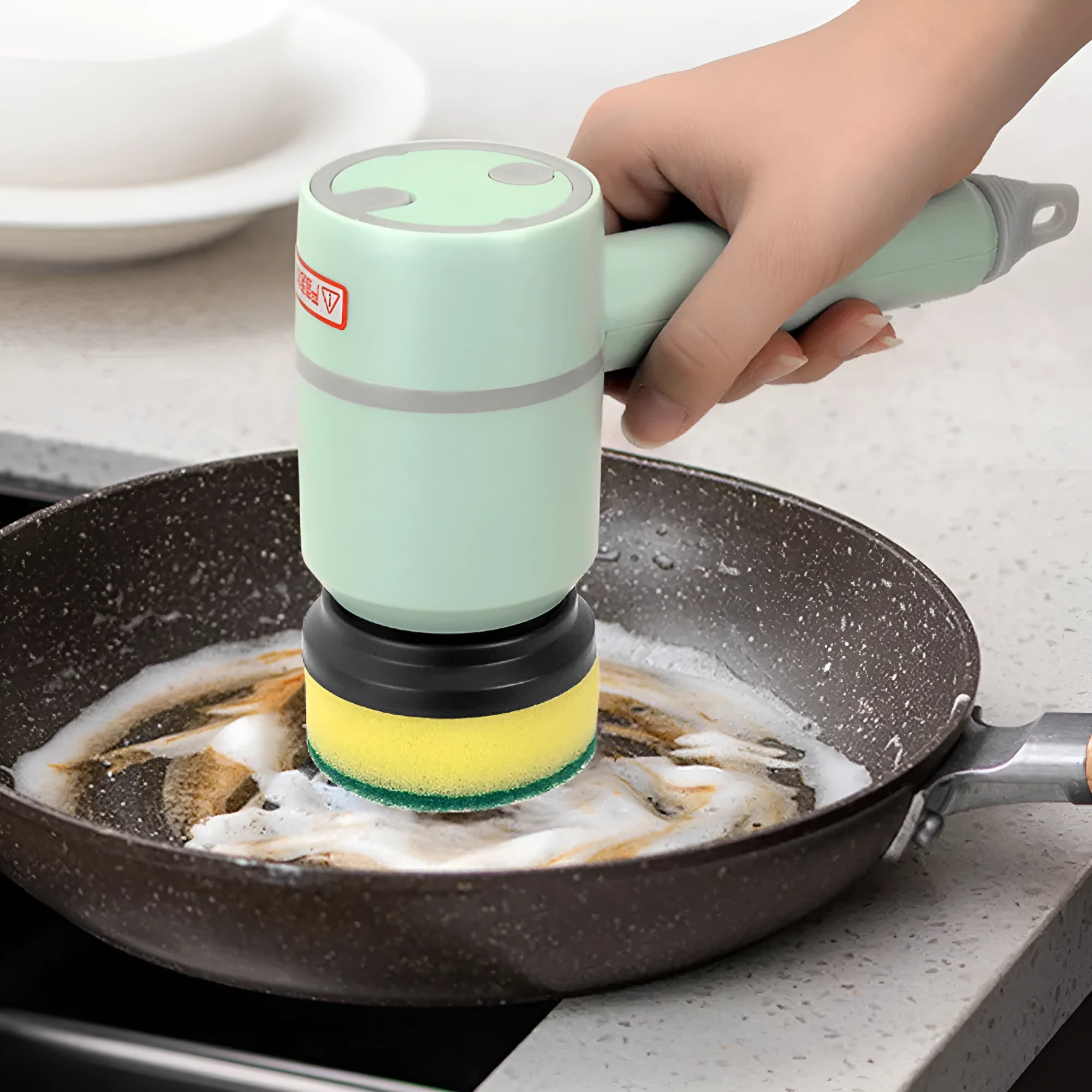 White rechargeable electric cleaning brush with multiple scrubber heads on a kitchen worktop.