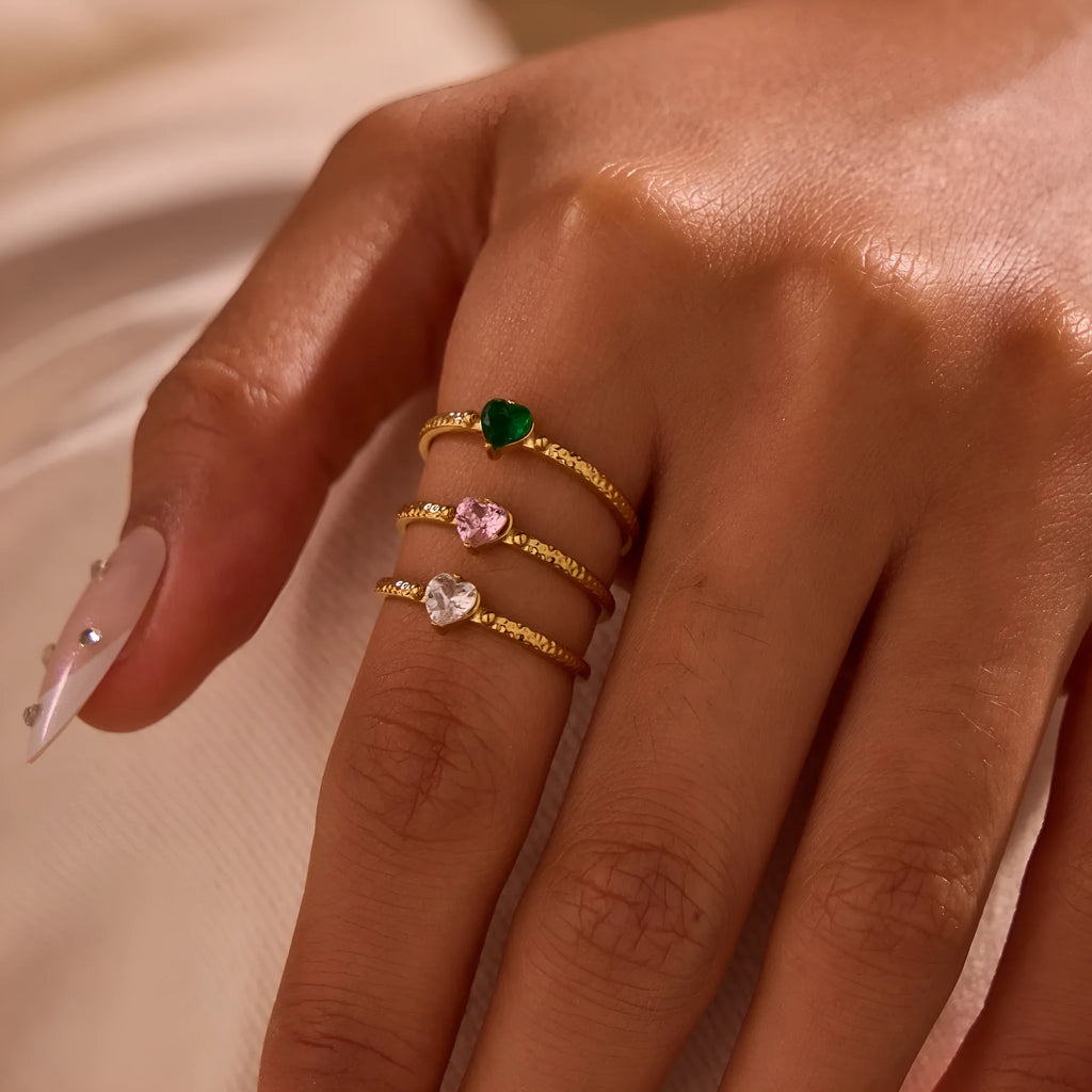 Open-ended geometric stainless steel ring with a heart-shaped green zirconium inlay on a grey background.