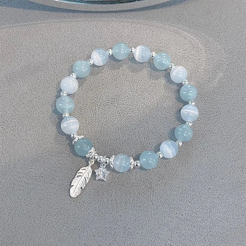 Small white crystal and glass charm bracelet with feather and blue moonlight details on wrist.