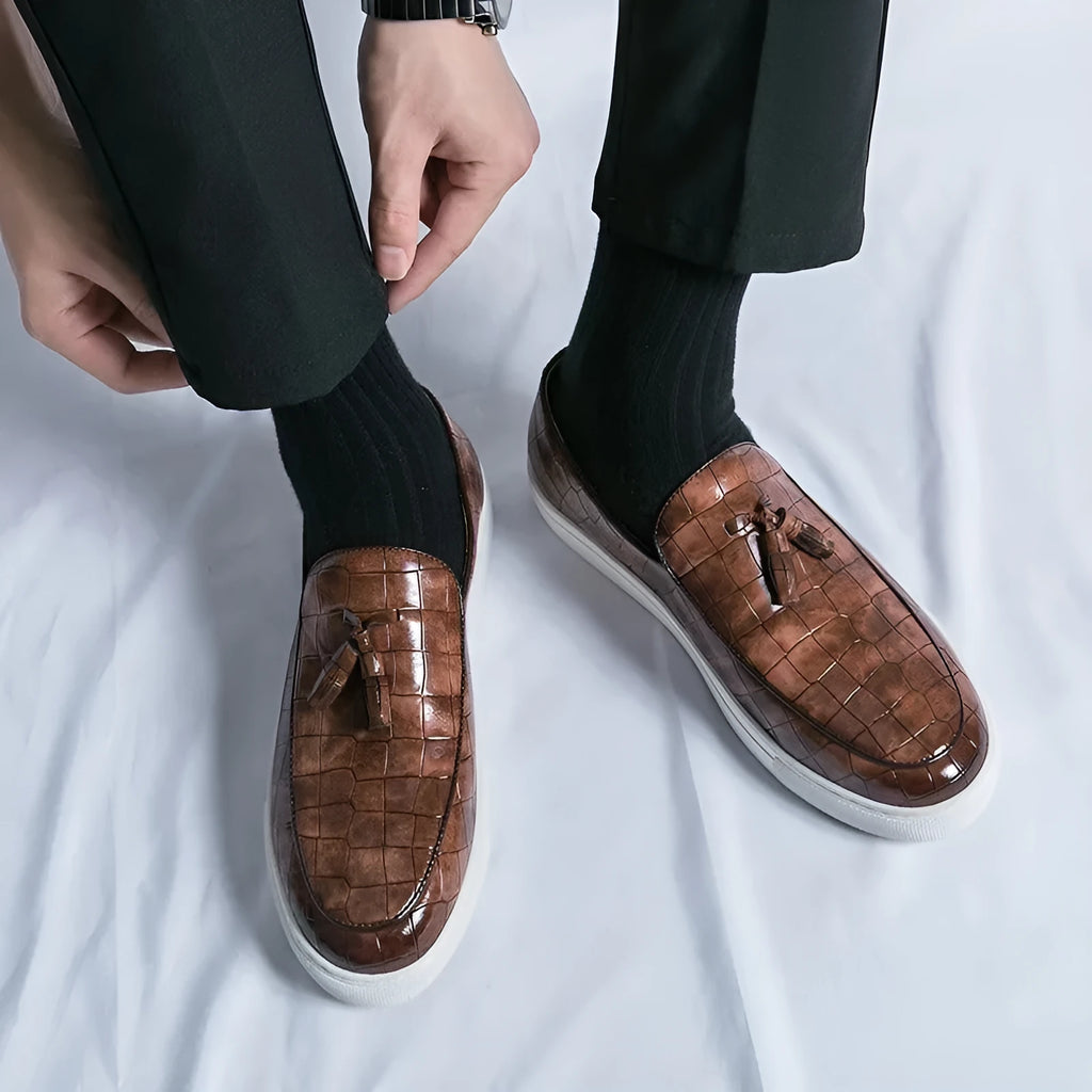 Men's black slip-on sneakers with a tassel detail on the round-toe upper.