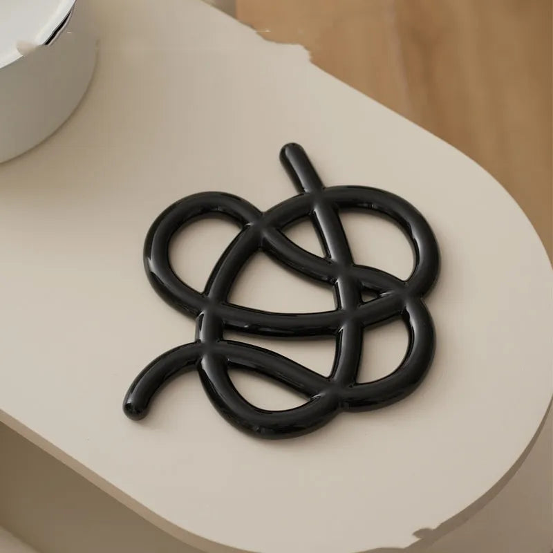 A ceramic heat-proof mat in an irregular shape on a table, shown in Bright Black, Coconut Milk Gray, and Splash Ink colour options.