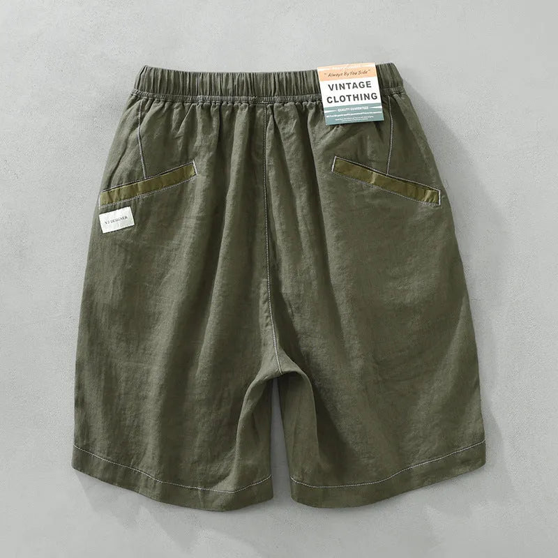 Man wearing loose green linen shorts with a drawstring waist and straight leg cut.