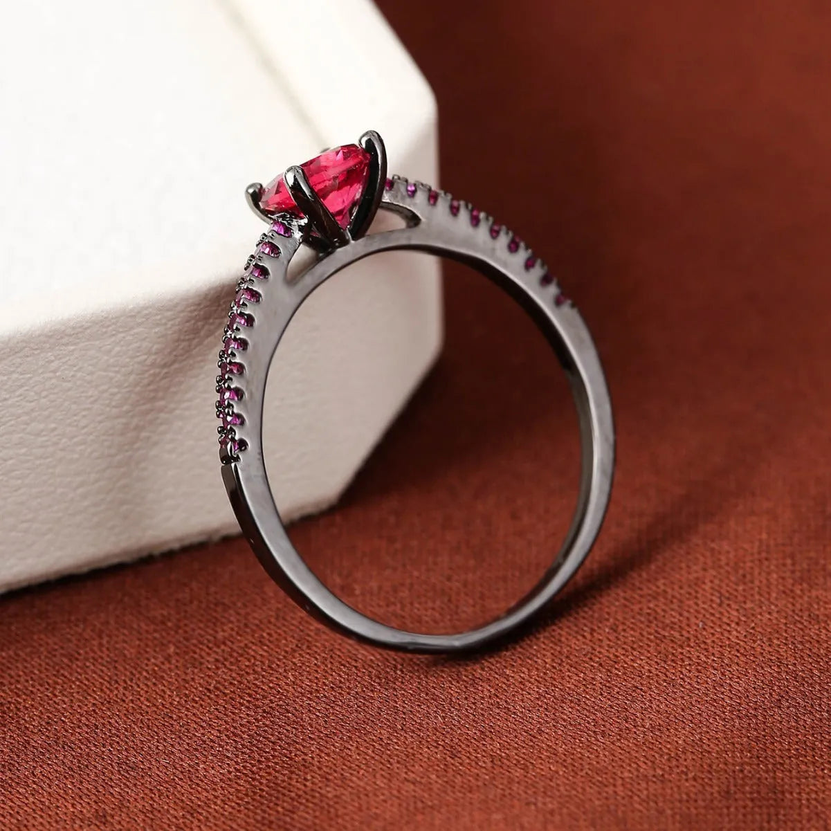 Colourful hexagon zircon copper ring in gold and gun black finishes on a size guide.