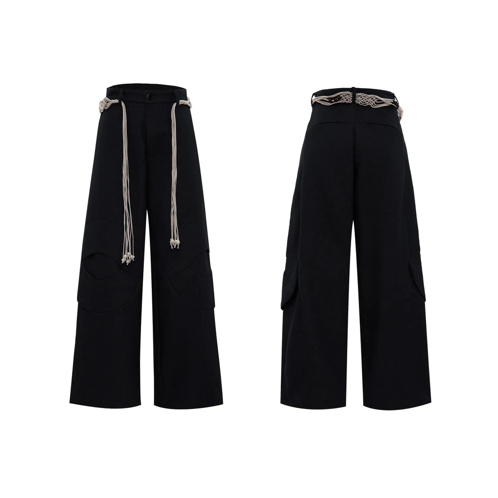 Men's dark coloured loose-fit straight-leg cotton trousers with decorative tassel and pocket zipper details.