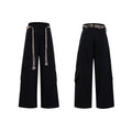 Men's dark coloured loose-fit straight-leg cotton trousers with decorative tassel and pocket zipper details.