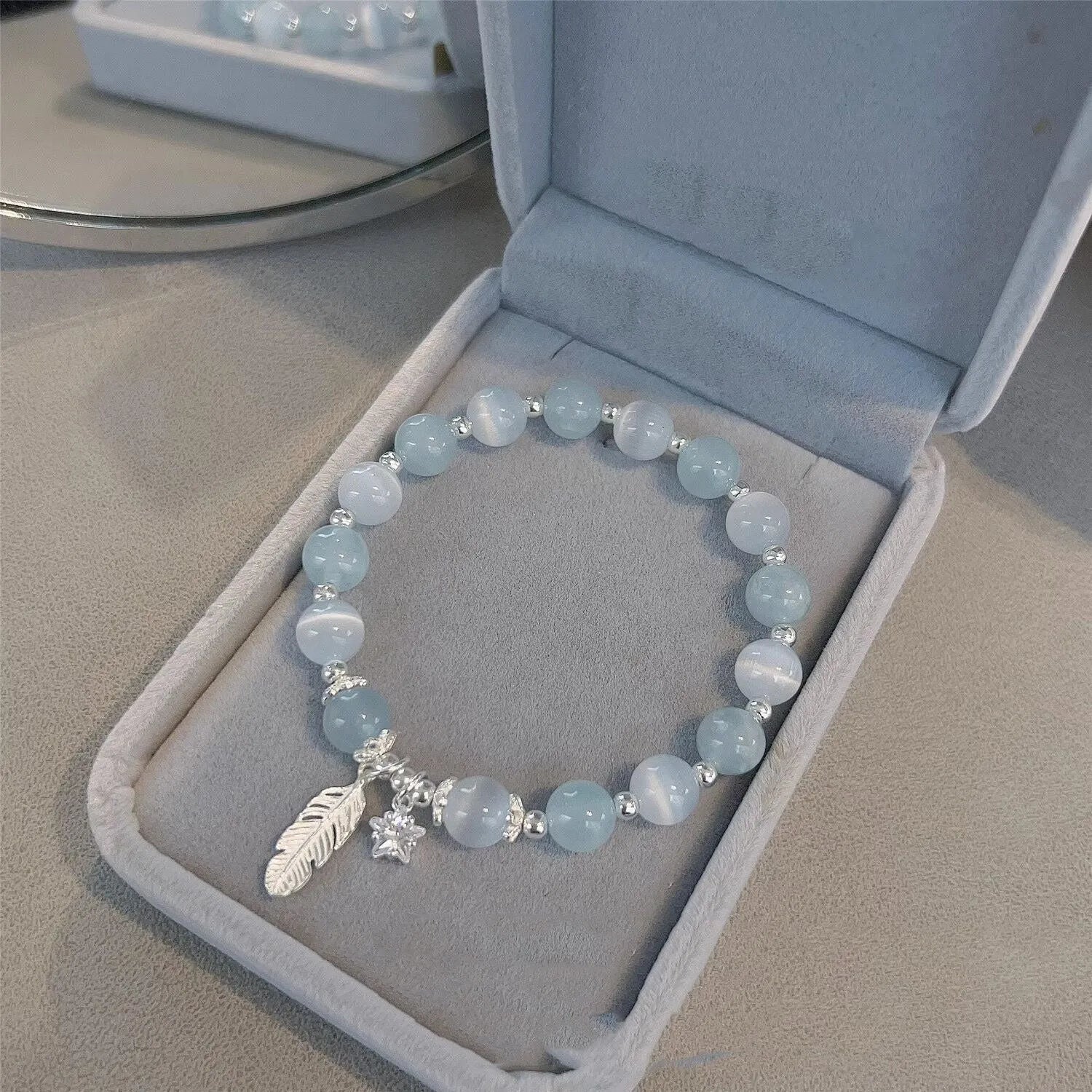 Small white crystal and glass charm bracelet with feather and blue moonlight details on wrist.