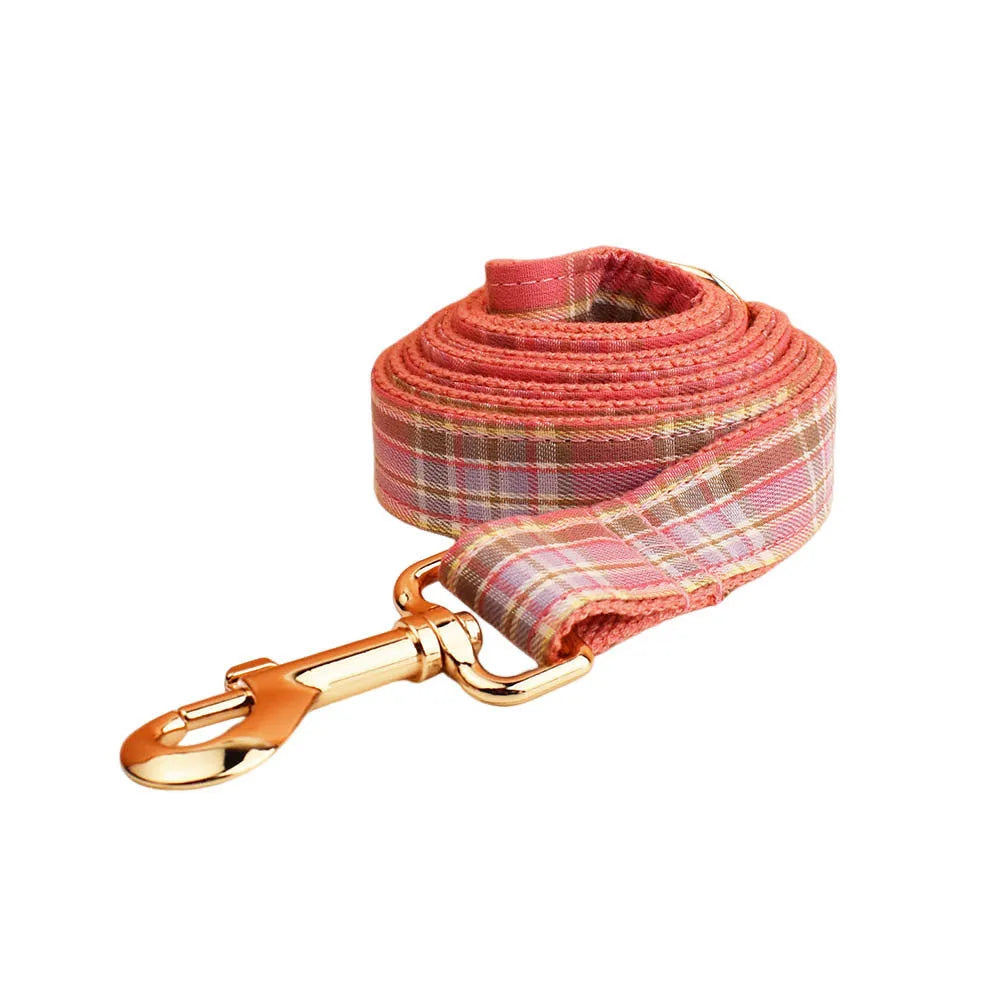 Plaid fabric dog collar, leash, bow, and vest four-piece accessory set on a white background.