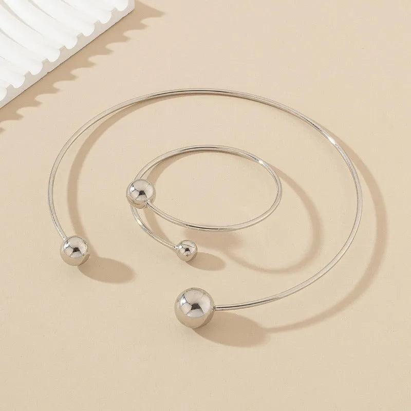 Gold dislocation ball open-end thin bangle bracelet with matching necklace on a flat surface