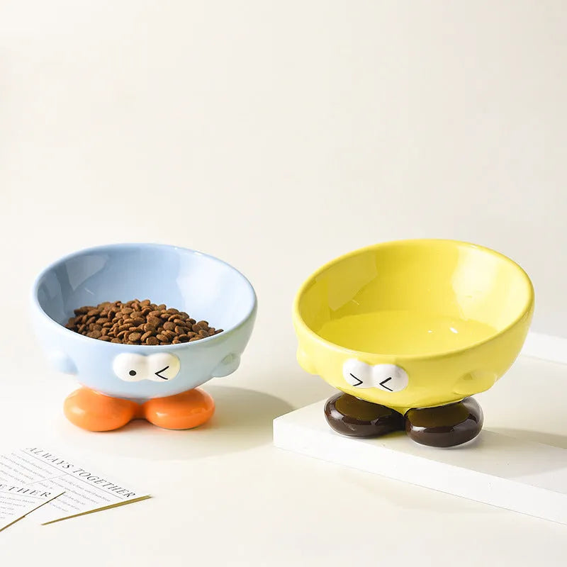 Blue and yellow ceramic slanted pet food bowls with animal face expressions for cervical spine support.