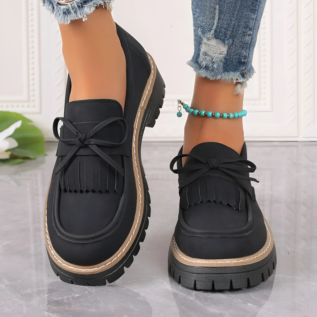 Black plus size women's loafers with a front bowknot and tassel on a chunky flat rubber sole.