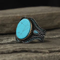 Men's antique silver alloy ring with a round band and a central turquoise stone on a finger.