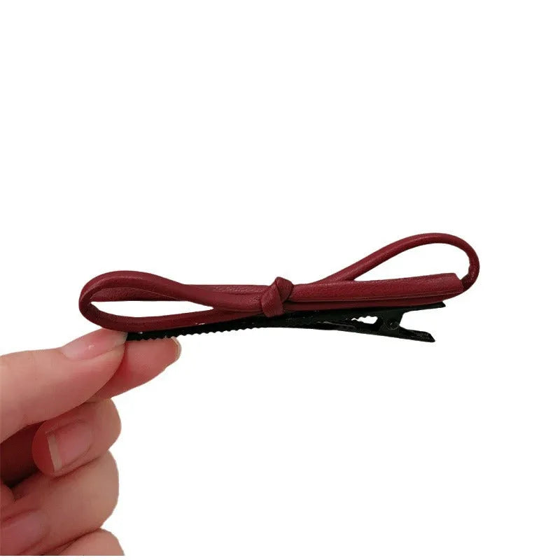 A wine red leather hair clip with a bow design, shown as a single barrette.