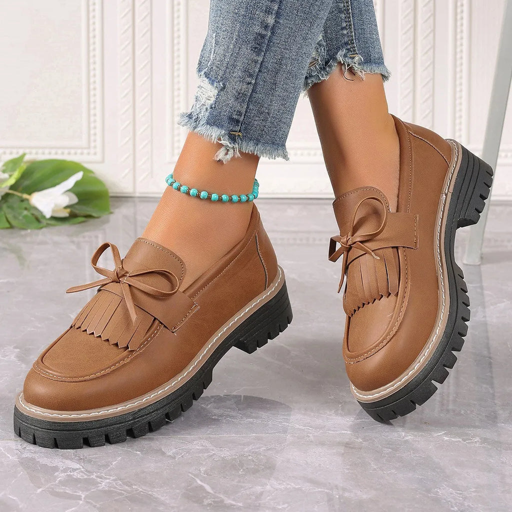 Black plus size women's loafers with a front bowknot and tassel on a chunky flat rubber sole.