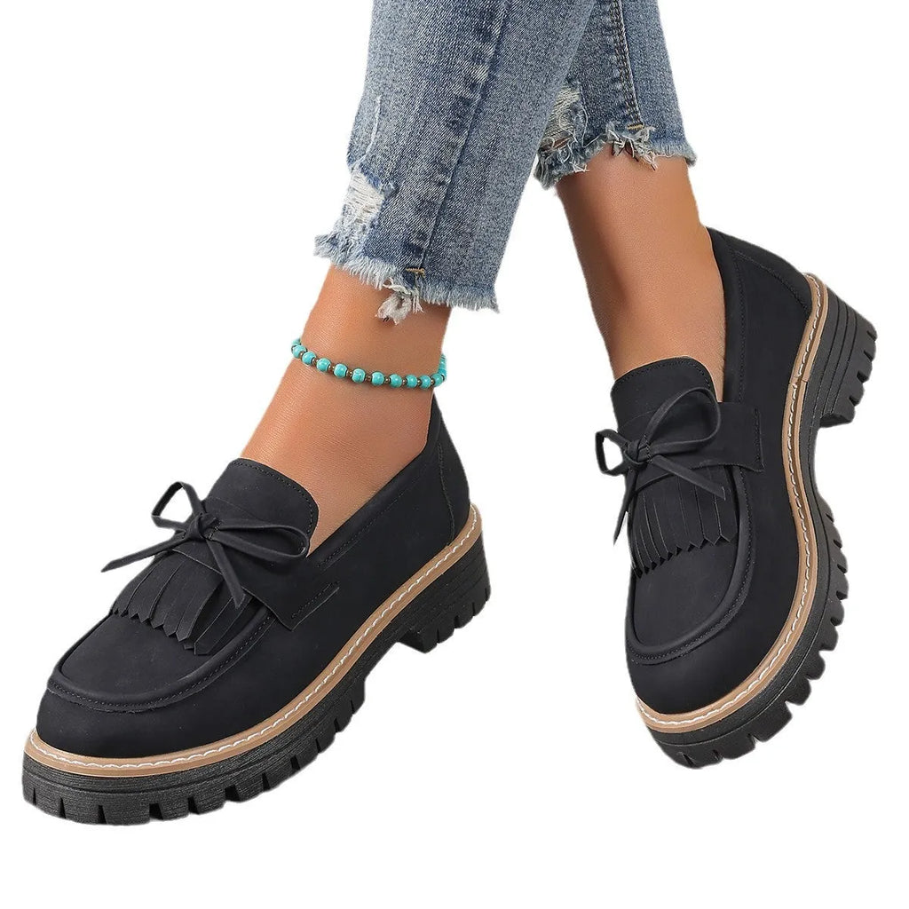 Black plus size women's loafers with a front bowknot and tassel on a chunky flat rubber sole.