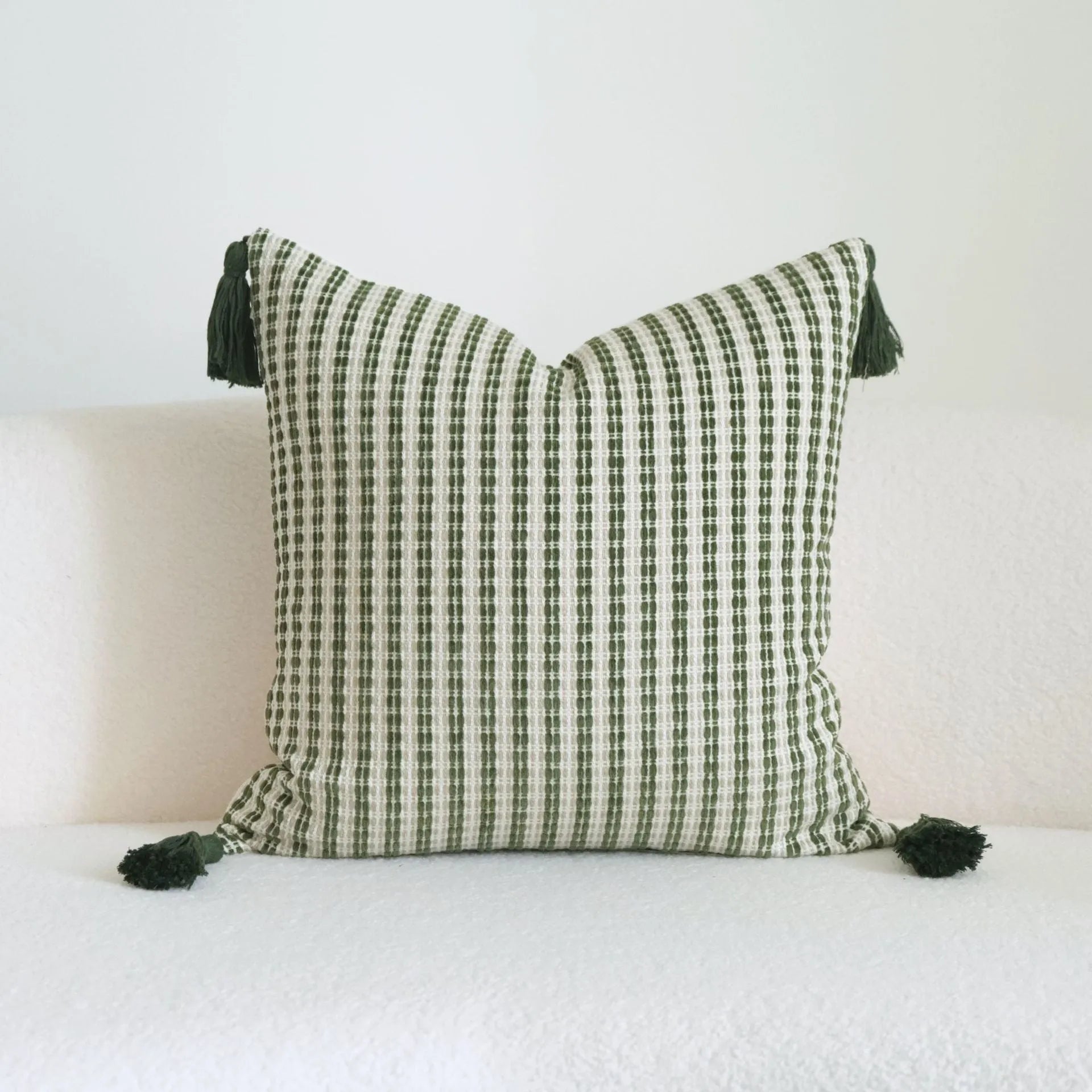 Green cotton and linen hotel pillow with tassel detail on a bed.
