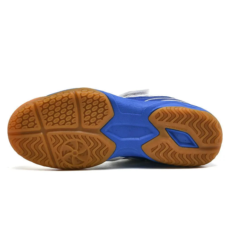 White and blue low-top badminton shoes with a ribbed sole and round toe on a hard court surface.