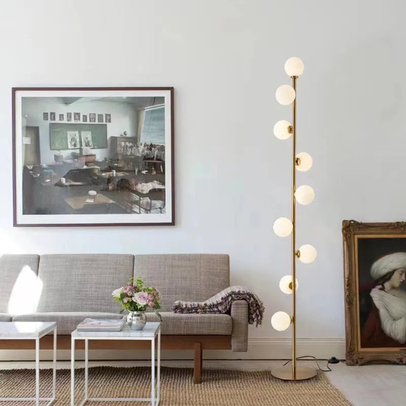 A tall modern minimalist floor lamp with a glass shade, wrought iron frame, and a grey marble base.