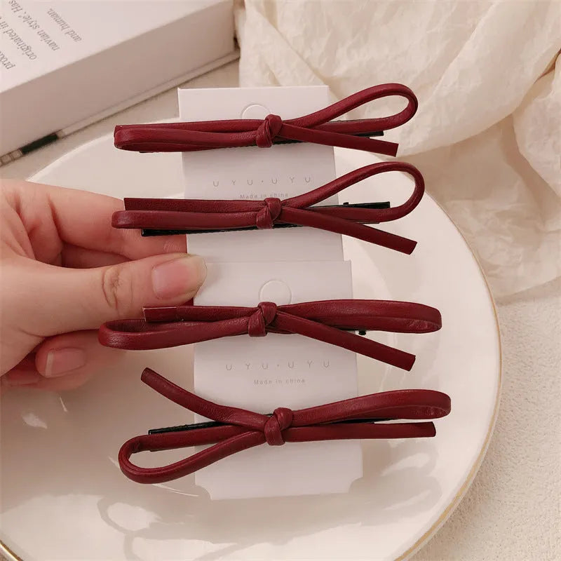 A wine red leather hair clip with a bow design, shown as a single barrette.