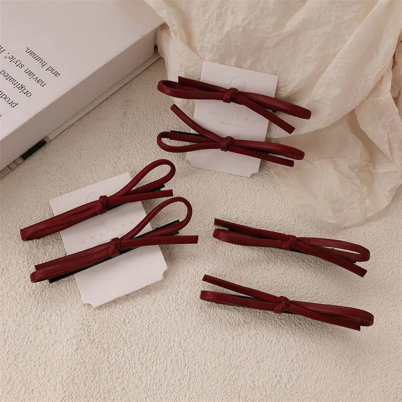A wine red leather hair clip with a bow design, shown as a single barrette.