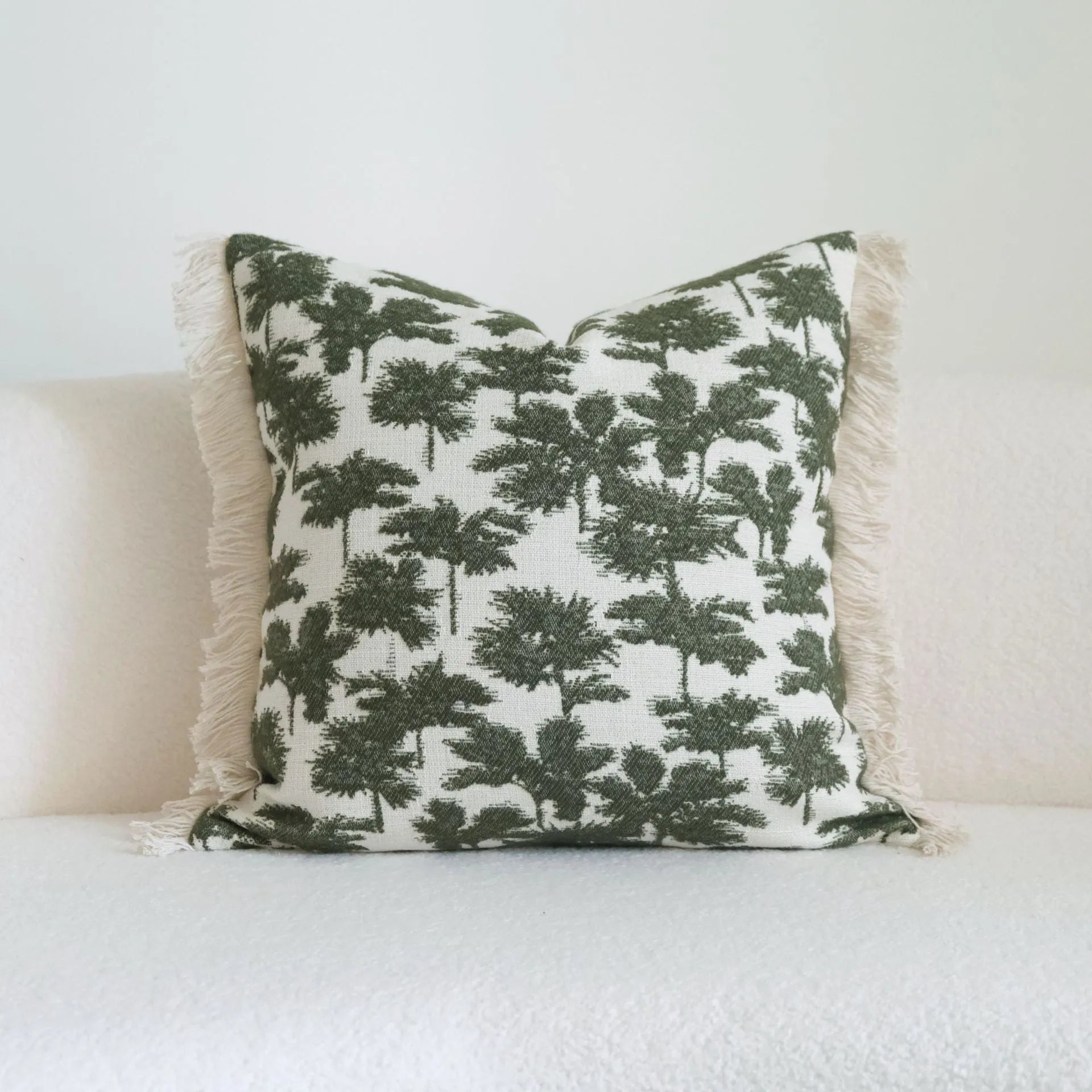 Green cotton and linen hotel pillow with tassel detail on a bed.