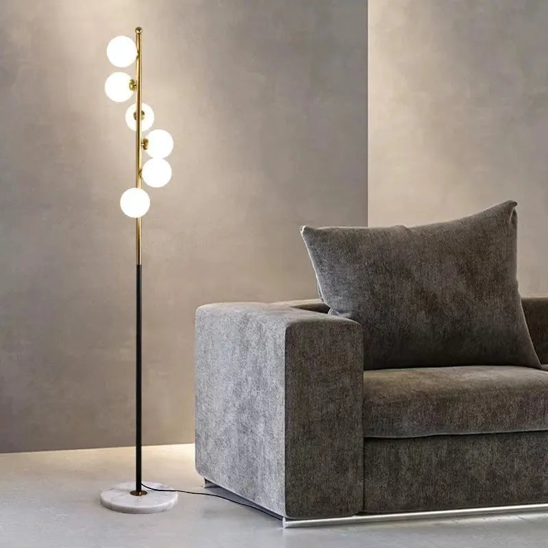 A tall modern minimalist floor lamp with a glass shade, wrought iron frame, and a grey marble base.