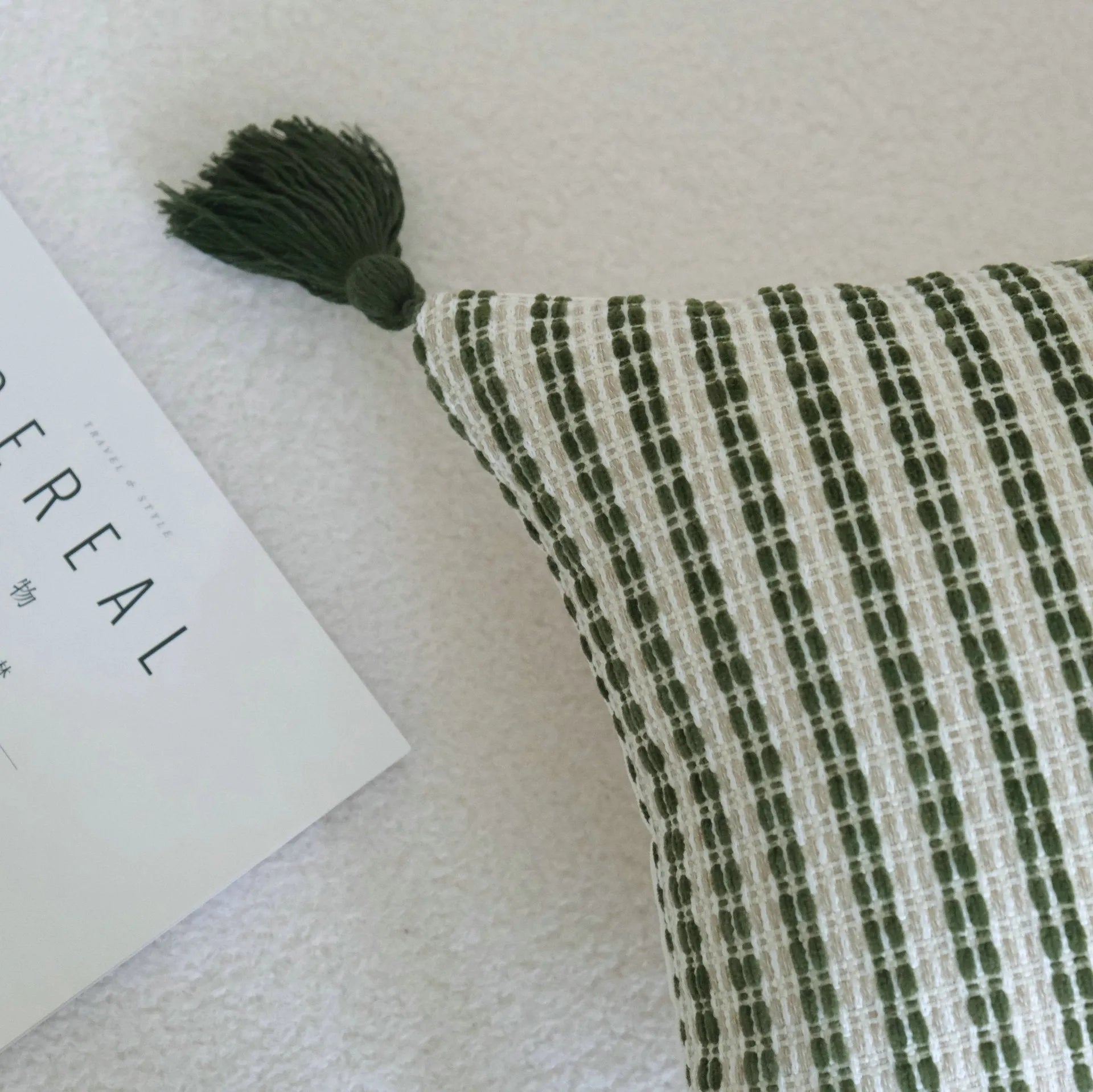 Green cotton and linen hotel pillow with tassel detail on a bed.
