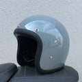 Retro-style open face motorcycle helmet in fibreglass, shown in a selection of colours including cement grey and matte black.