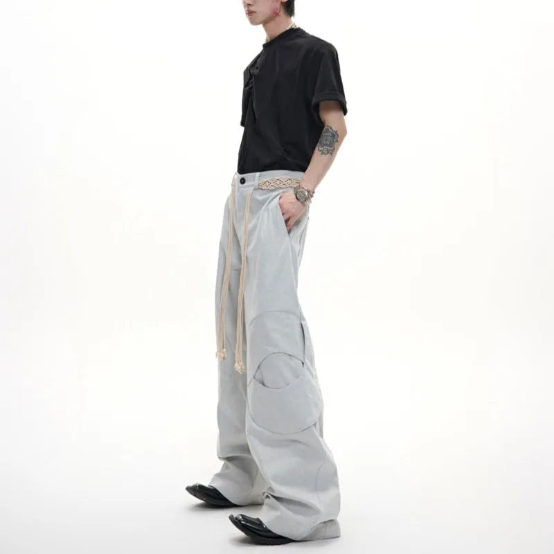 Men's dark coloured loose-fit straight-leg cotton trousers with decorative tassel and pocket zipper details.