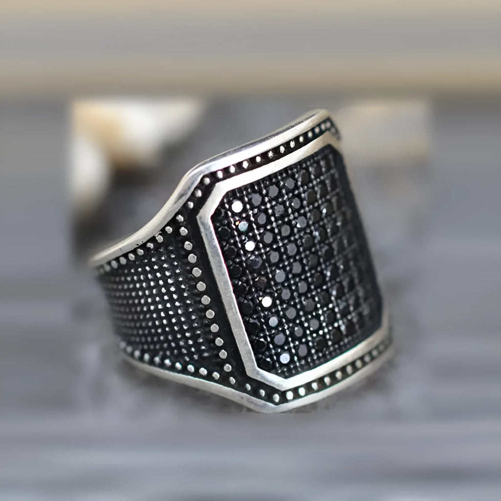 Black geometric alloy ring with copper inlay and zircon stone details on a finger.