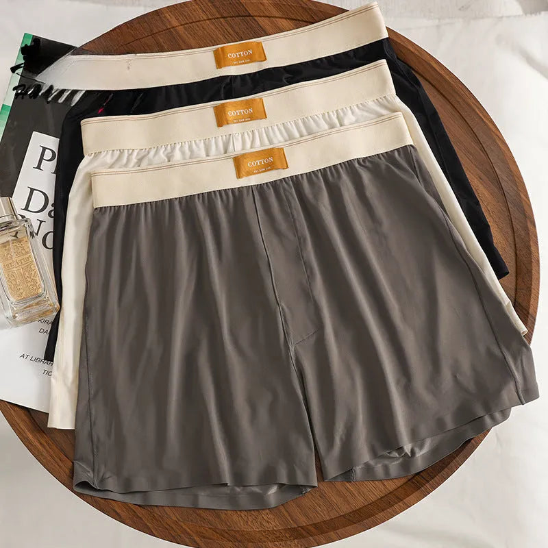 Three pairs of solid colour men's loose fit ice silk boxers laid flat, showing beige apricot, black, and dark grey.