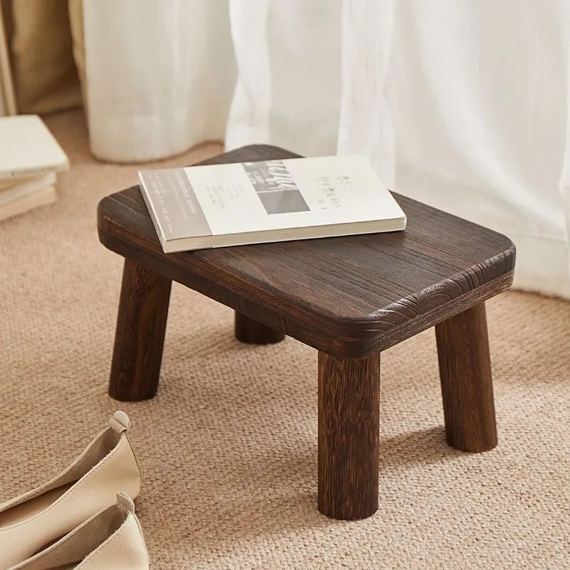 Distressed solid wood shoe stool with bracket legs in a living room setting.