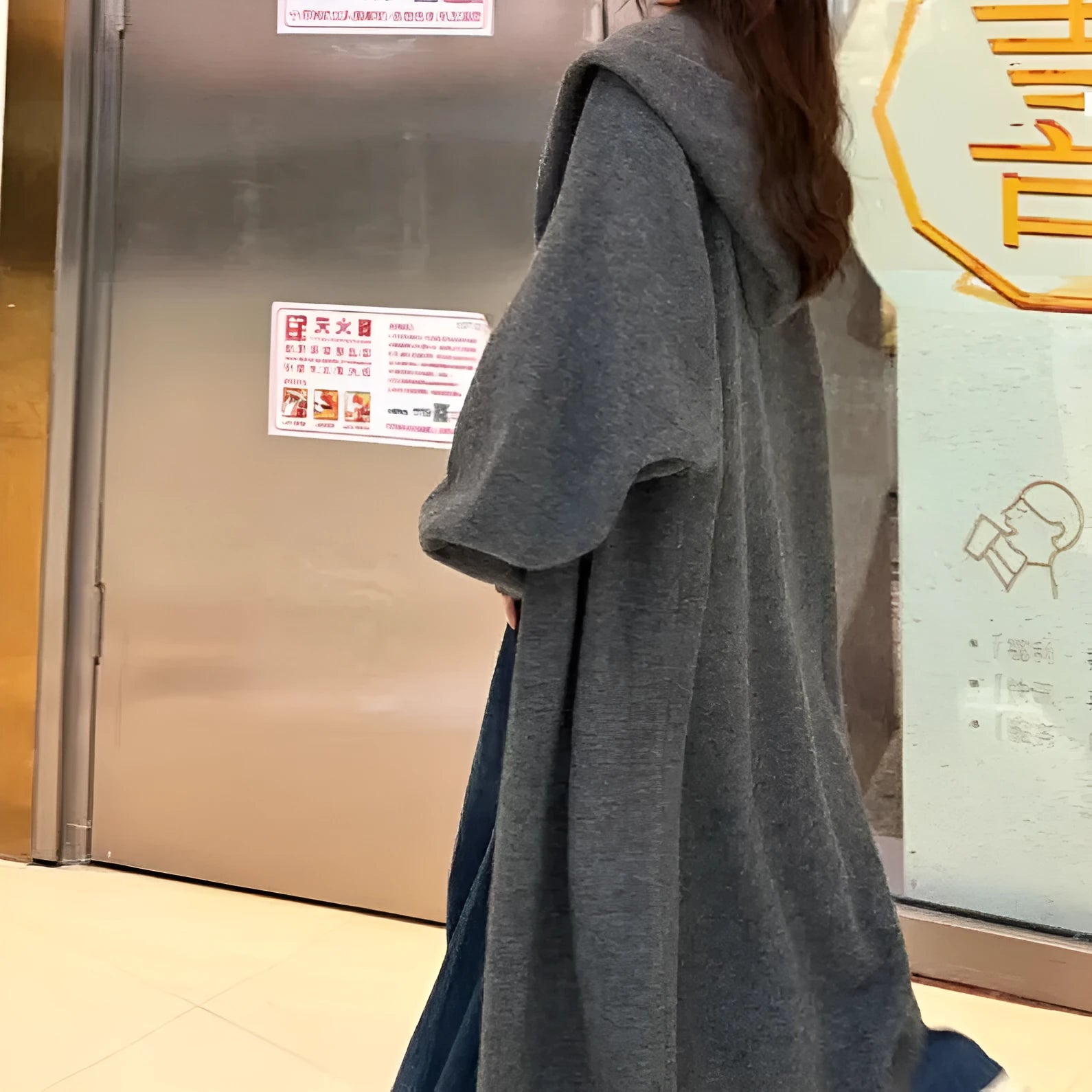 A woman wearing a long, loose, hooded knitted cardigan in a solid colour, demonstrating its below-the-knee length.